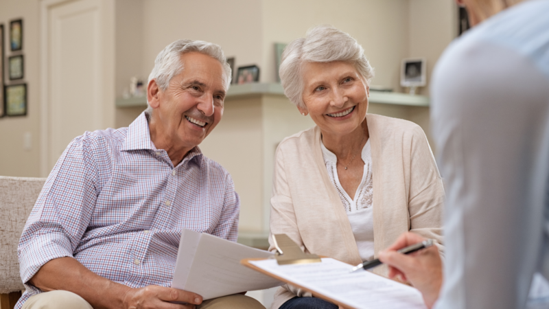Smiling retired couple discussing finances with an advisor, representing guidance on how much is needed to retire comfortably