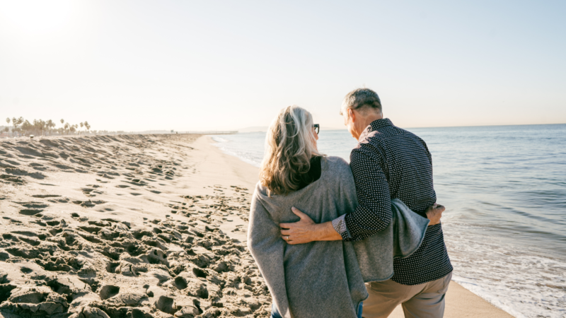 Smiling couple walking along the beach, representing the freedom and security of over 50s life insurance